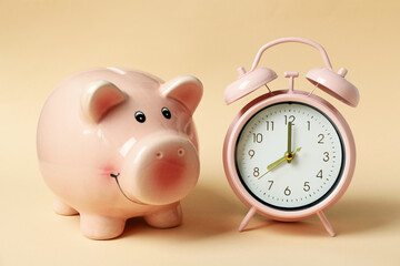 Piggy bank and pink alarm clock on beige background