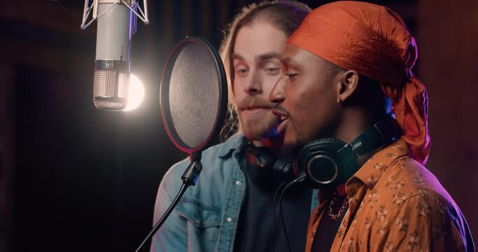 Two Handsome Singer Recording Music Hit together in Modern Record Studio. Wears Stylish Clothes enjoys Collaboration. Talented Musicians preparing for Concert. Professional Microphone. Future Success.