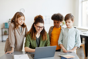 Portrait of young female teacher using computer with diverse group of children