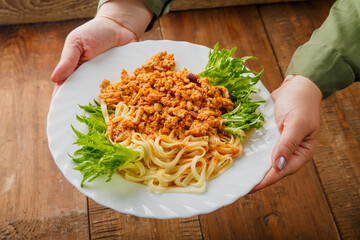 A plate of pasta in bolognese sauce in female hands.