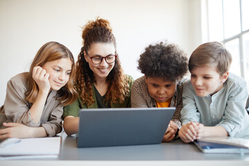 Portrait of smiling female teacher using computer with diverse group of children