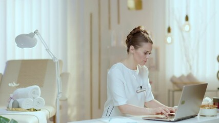 tired female employee with laptop having neck pain in modern beauty studio. This video was made with PRORes 422 codec.