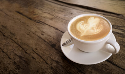 Top view of flower latte art in a cup of cappuccino on blurred background of an old wooden table. Beautiful heart shaped milk foam in a white cup of hot coffee. The dark tone and vintage image.
