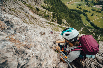 Well-equipped woman and man mountaineers climbing a rocky route with magnificent views of the mountain and the valley with the trees and paths
