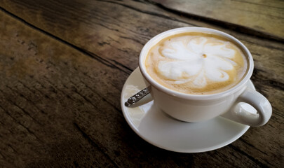 Image of flower latte art in a cup of cappuccino on blurred background of an old wooden table. Top view of hot coffee in a white cup with beautiful foam. The dark tone and vintage image.