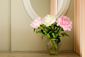 Studio shot of beautiful peony flowers in a glass vase on a table over gray wall background with a lot of copy space for text. Feminine floral composition. Close up, backdrop.