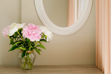 Studio shot of beautiful peony flowers in a glass vase on a table over gray wall background with a lot of copy space for text. Feminine floral composition. Close up, backdrop.
