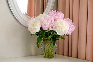Studio shot of beautiful peony flowers in a glass vase on a table over gray wall background with a lot of copy space for text. Feminine floral composition. Close up, backdrop.