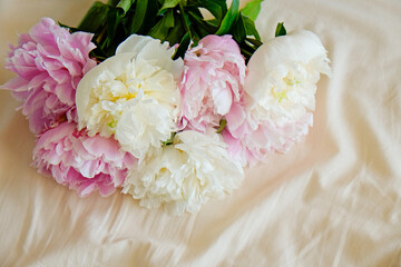 Close up shot of pink and white peony flowers on an unmade bed. Copy space for text, top view, background.