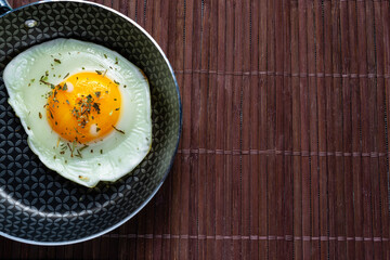 Frying pan with fried egg on a bamboo table