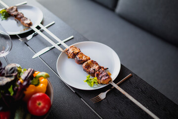 Fried meat on a skewer.Shish kebab on a plate.Skewer with a kebab and a glass of wine.Dinner on the terrace with wine and meat.Fried meat for dinner.Meat.Covered dinner.Delicious food on the table.Sum