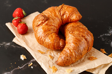 Fresh baked butter breakfast croissants and crumbs  and strawberries on paper