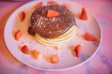 Portion of sweet pancakes filled with chocolate and surrounded by strawberry slices on pink plate. Concept of home-made food. Proper nutrition. Pleasure and pleasure.