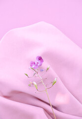Purple flower on pink silk fabric background. Aesthetic minimal wallpaper. Summer Spring floral plant composition