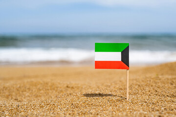 Fototapeta na wymiar Flag of Kuwait in the form of a toothpick in the sand of beach opposite sea wave. Travel concept