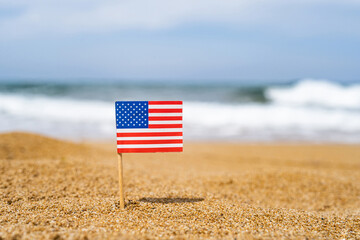 Flag of America in the form of a toothpick in the sand of beach opposite sea wave. Travel concept