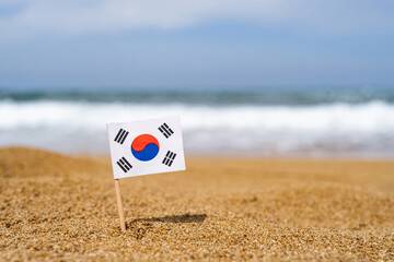 Flag of South Korea in the form of a toothpick in the sand of beach opposite sea wave. Travel...