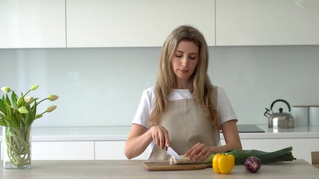 Women cuts organic fresh leeks on the wooden cutting board. Cooking at home.