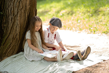 Children sit on a blanket by a large tree and read a book