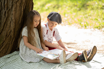 Children sit on a blanket by a large tree and read a book