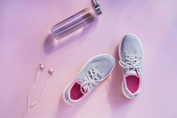Top view sneakers, earphones and glass water bottle on a pink background. Set for running and sports activities. Healthy and active lifestyle. Online workout. Flat lay. Copy space.
