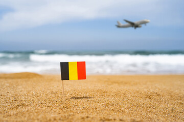 Flag of Germany in the form of a toothpick in the sand of beach opposite sea wave with landing airplane. Travel concept