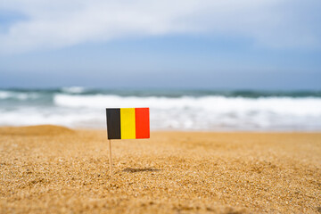 Flag of Germany in the form of a toothpick in the sand of beach opposite sea wav. Travel concept