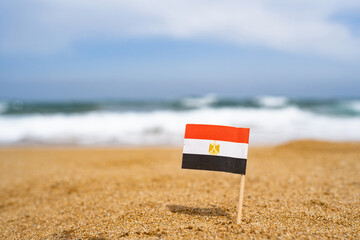 Flag of Egypt in the form of a toothpick in the sand of beach opposite sea wave. Travel concept
