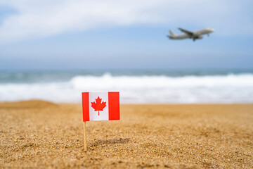 Flag of Canada in the form of a toothpick in the sand of beach opposite sea wave with landing...