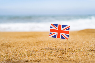 Flag of United Kingdom in the form of a toothpick in the sand of beach opposite sea wave. Travel...
