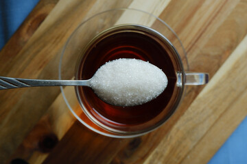 someone adds a spoonful of sugar to a glass of tea