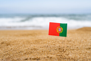 Flag of Portugal in the form of a toothpick in the sand of beach opposite sea wave. Travel concept