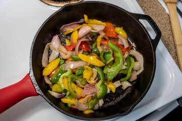 view of shrimp and peppers cooking in a cast iron skillet on a white stove top