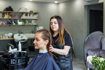 A girl in a beauty salon, a hairdresser does her hair, cuts her hair to a girl with long hair. a woman dyes her hair, dries her hair with a hair dryer