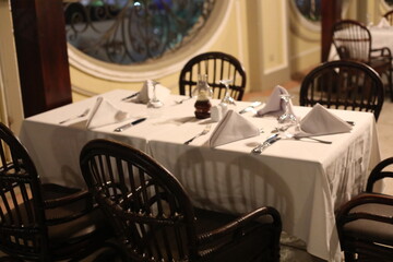 Table setting for a romantic dinner. Scenic cafe interior with modern service. Beautiful view of empty summer terrace. Serving tables near fountain in the evening light. Concept of resort culture.