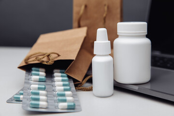 Online pharmacy concept. Pills and spray white mockup containers and buff paper bags over the laptop close-up