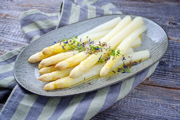 Modern style traditional steamed white asparagus garnished with butter sauce and herbs served as...