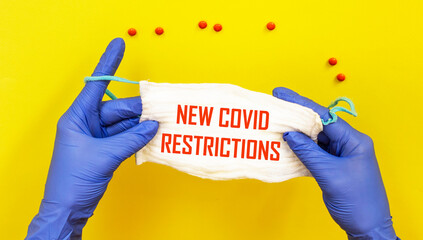 Text of new covid restrictions on a medical mask in the hands of a doctor in gloves.Medical concept.