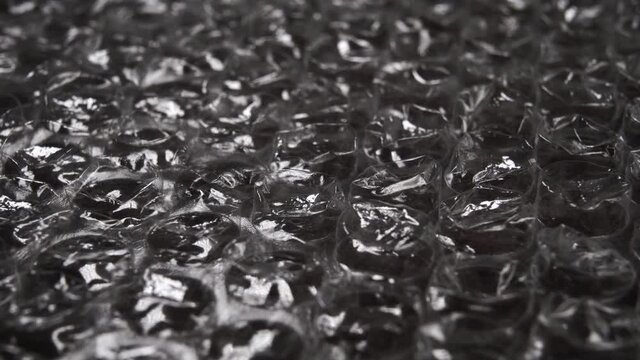 Black bubble wrap glitters and rotates. Macro shot. Recycled polyethylene material for fragile parcels. Abstract detailed dark background. Selective focus