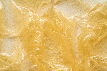 Transparent smear and texture of golden cosmetic gel on a white background.