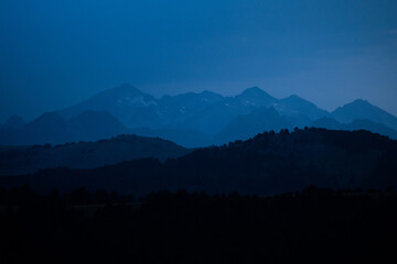Mountains layers during blue hour. Landscape with dark blue misty silhouettes of alpine mountains and fir trees forest in Pyrenees.