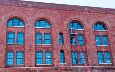 Window Washer on Crane Cleaning Windows of Large Brick Building
