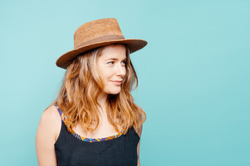 Happy young blonde girl not looking at camera with straw hat on blue background. Summer concept. copy space.
