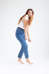 young attractive caucasian woman with long hair in t-shirt and blue jeans dances on white studio background. skinny pretty female dancing on cyclorama with bare feet. model tests of beautiful lady