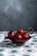 Dark photography of plums on a retro pattern tablecloth. Moody picture of seasonal fruit with copy space.
