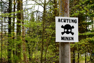 An old abandoned sign saying ACHTUNG MINEN (CAUTION! MINES) in German hanging from a small concrete...