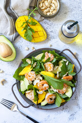 Healthy diet salad with arugula, spinach, mango, avocado, shrimp, pecans and vinaigrette dressing on a gray stone table top. Top view flat lay background.