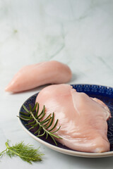 Raw chicken breast without skin, with herbs in a blue plate, green background

