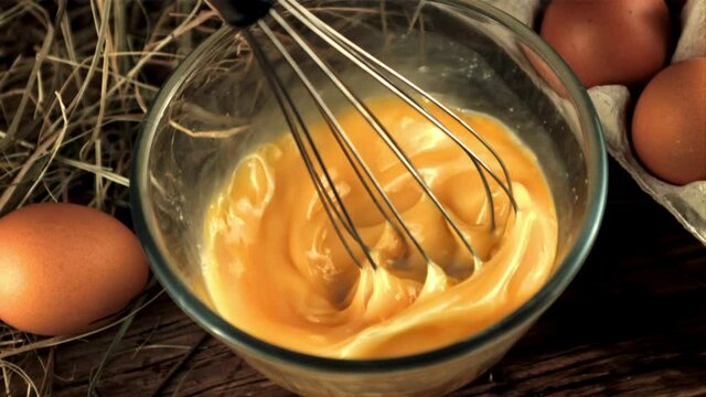 Super slow whisk movement stirred eggs for breakfast preparation. On a wooden background. Filmed on a high-speed camera at 1000 fps.