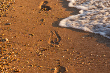 Footprints of the golden sand beach. Small waves roll up on the shore and wash away the tracks. The man walked along the beach. Summer textured background. The concept of rest, relaxation, privacy.